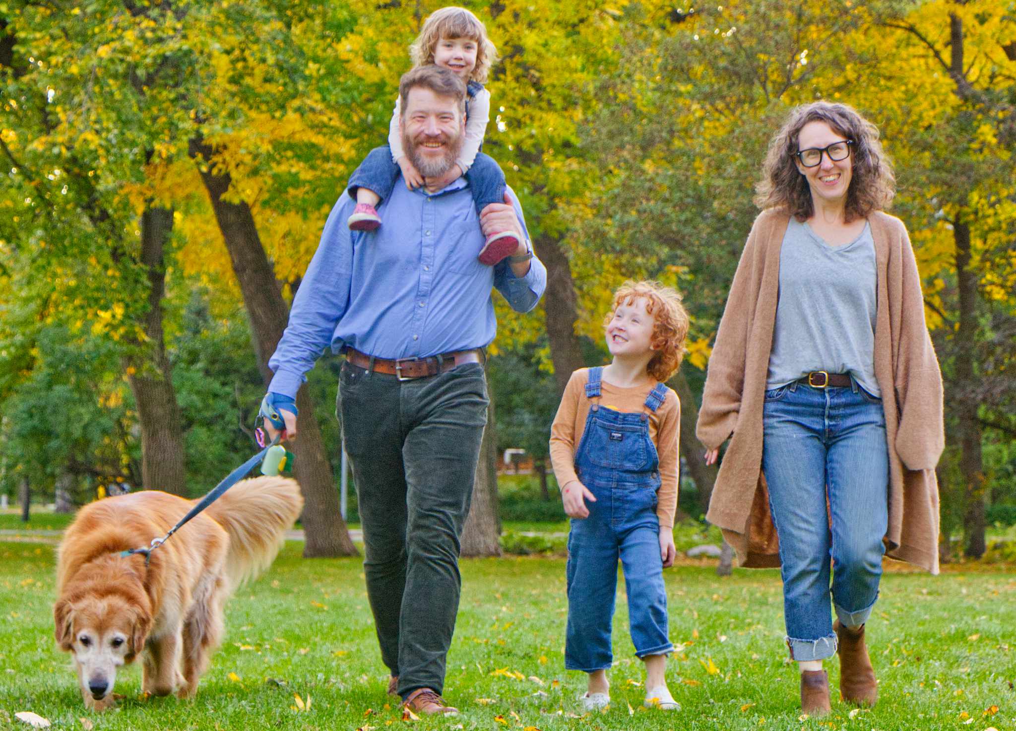 Andrew Kohan, a white man with a beard, walks in a park with two children, a woman, and a large dog.