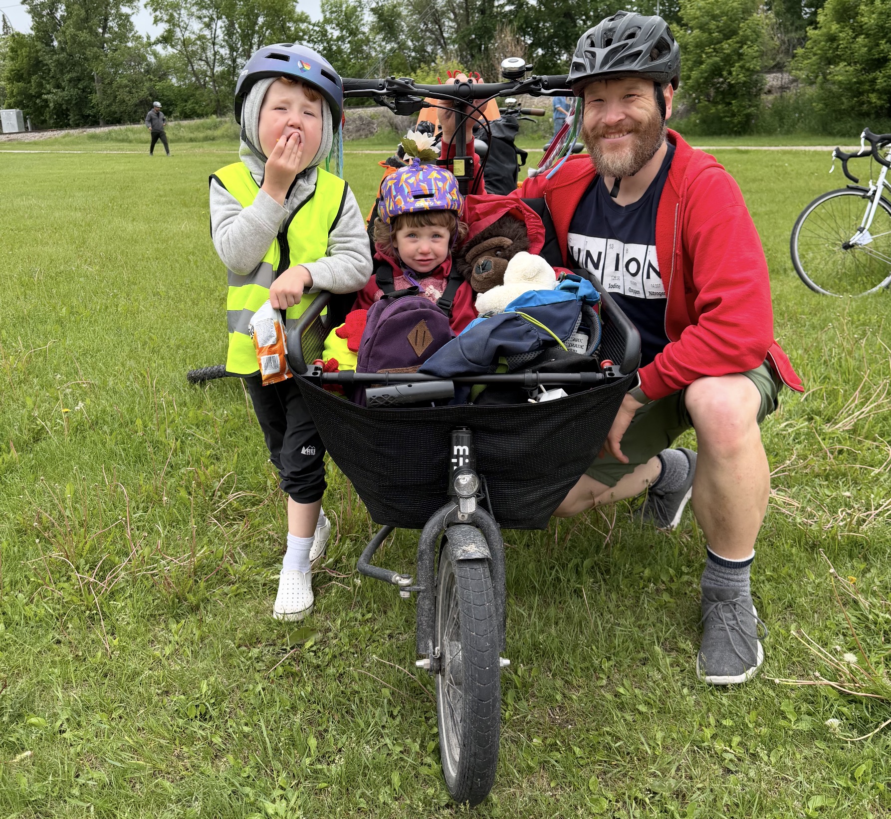 andrew Kohan, a white man with a beard, wearing a bike helmet and holding a cargo bike with two children